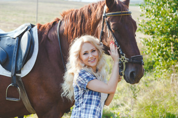 Beautiful blonde girl in plaid shirt hugging her brown horse