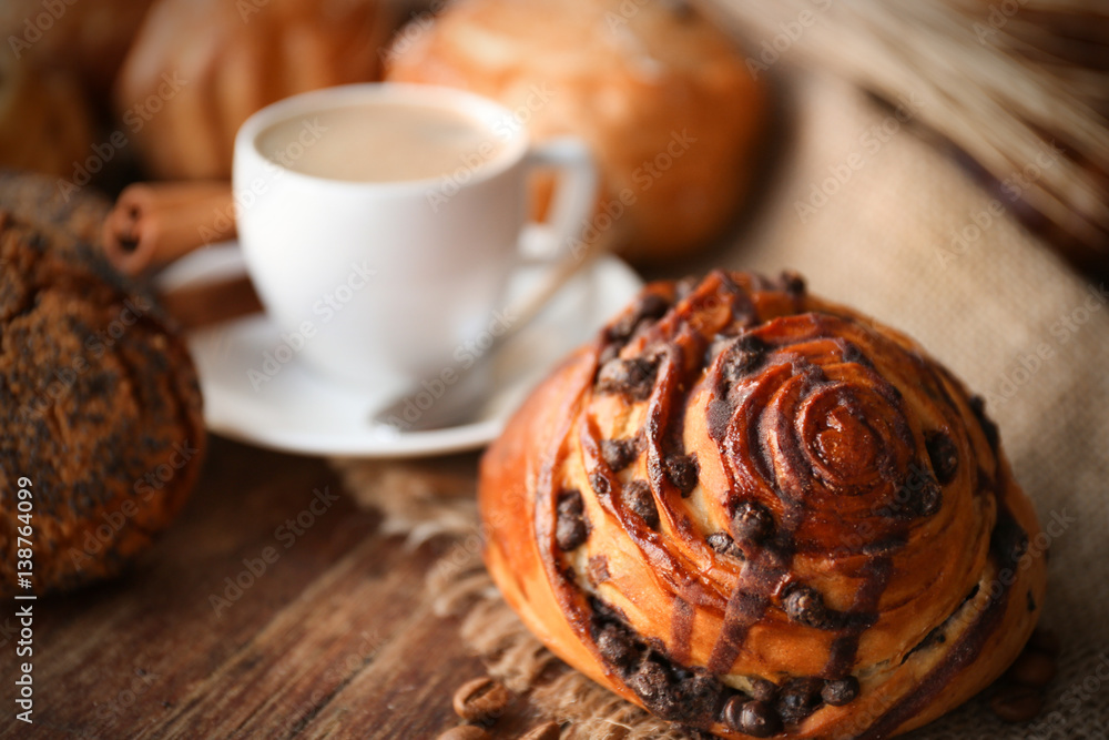 Tasty bun with cup of coffee on table, close up