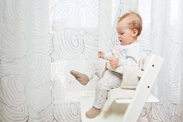 Wall Mural - Eleven months old baby girl sitting in a stool looking at her feet