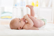 © Oksana Kuzmina - Funny little baby wearing a nappy playing with his legs in nursery. Cute kid sucking his feet. Child after bath or shower on bed. Infant skin care.