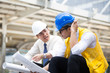 © Bavorndej - Engineers sitting in front of building with blueprint on hand,Businessman,Engineers reading in blueprint instructions on hand in front of building