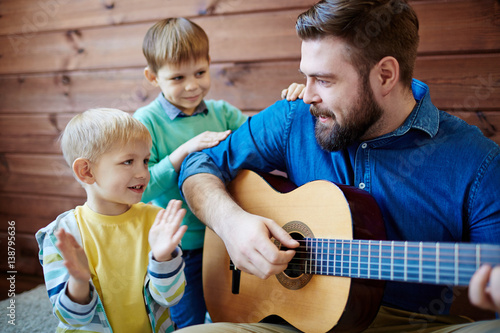 Fotografía Bearded nursery teacher giving music lesson to little boys: he playing guitar an
