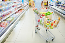 Young Woman On Healthy Diet With Shopping Cart Full Of Fresh Vegetables, Fruits And Dairy Products Posing In Supermarket