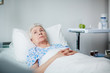 Lonely senior woman lying thoughtful on white sheets in hospital ward