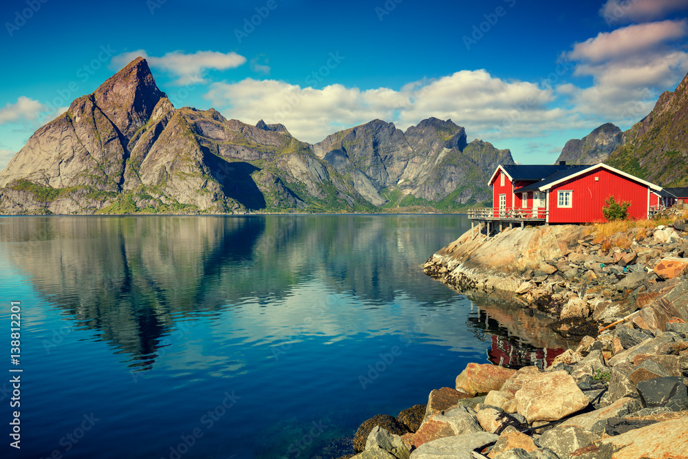 Beautiful fishing village on fjord. Beautiful nature with blue sky, reflection in water, rocky beach and fishing house (rorby). Lofoten, Reine, Norway - obrazy, fototapety, plakaty 