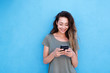 © mimagephotos - young smiling woman using mobile phone against blue background