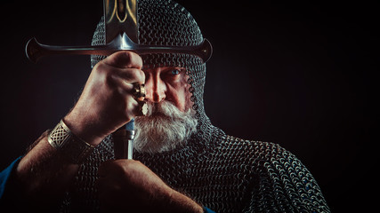 Powerful bearded knight with the sword on the dark background