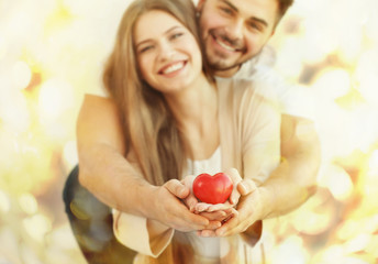 Poster - Young couple holding small red heart, on light background