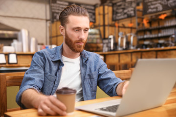 Handsome young man working on computer at cafe