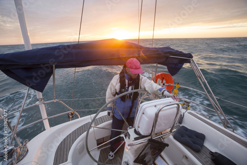 Fotomural Man Standing At Helm Of Yacht Sailing In Sea During Sunset