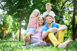 © vitaliymateha - young happy family at noon in the park on the grass. Two young parents and children, boy and girl, sits on the grass and smiling looking at the camera.