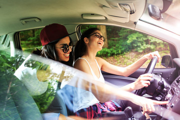 Two young female on car trip.They are driving the car and making fun.Positive emotions.