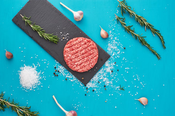 Fresh raw beef meat with herbs and salt on turquoise background. Flat lay.