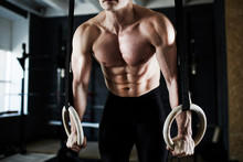 Intense Crossfit Workout In Dark Gym: Closeup Shot Of Ripped Male Torso With Defined Muscle Pattern On Chest And Arms During Gymnastic Rings Exercise