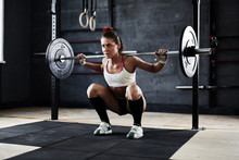 Intense Crossfit Workout In Dark Gym: Strained Young Sportswoman Ready To Perform Shoulder Press Exercise With Heavy Barbell