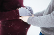 Woman holds man's hands on her pregnant belly standing under falling snow