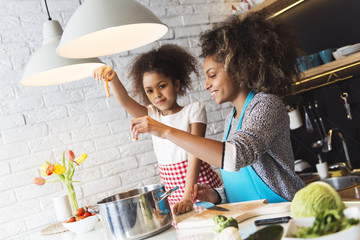 Beautiful African American woman and her daughter cooking in the kitchen 