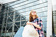 © Iryna - Young female student in sunglasses looking forward and holding hat and paper bag before modern buildsng of airport terminal.