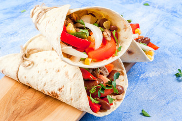 Wall Mural - Street fast Mexican food, freshly prepared, homemade sandwiches burrito with beans, beef, corn, peppers, tomatoes and herbs. On the blue background of the concrete stone, close view copy space