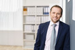© contrastwerkstatt - erfolgreicher geschäftsmann lehnt sich lässig an einer wand im büro