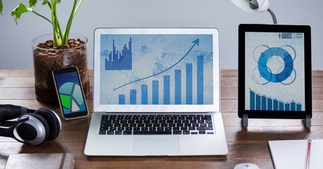 Sticker - Laptop and digital tablet with graph charts on wooden table