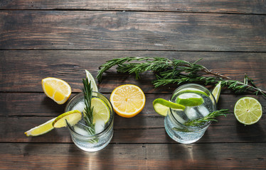 Wall Mural - Alcoholic drink gin tonic cocktail with lemon, rosemary and ice on rustic wooden table, copy space.