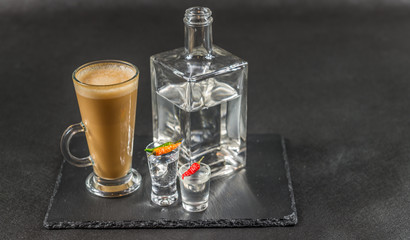 aromatic coffee latte with vodka in a decanter and two glasses decorated with peppers, whole black stone plate