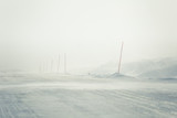 Fototapeta Na ścianę - A beautiful landscape with a white, snowy road with safety poles in the Norwegian winter