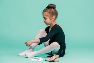 beautiful little ballerina in black dress for dancing puting on foot pointe shoes