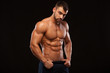 Strong Athletic Man - Fitness Model showing Torso with six pack abs. stands straight and puts his hands in trousers. isolated on black background with copyspace.