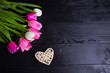 Bouquet of tender pink tulips and wicker heart on black wooden background
