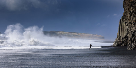 Wall Mural - Man walking on Vik black beach, looking at giant waves - breathtaking Iceland in winter - amazing landscapes, storms and blizzards - photographers paradise