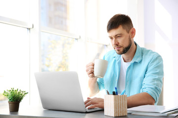 Sticker - Handsome young man drinking coffee while working with laptop at home