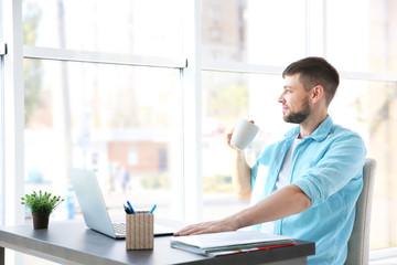 Sticker - Handsome young man drinking coffee while working with laptop at home