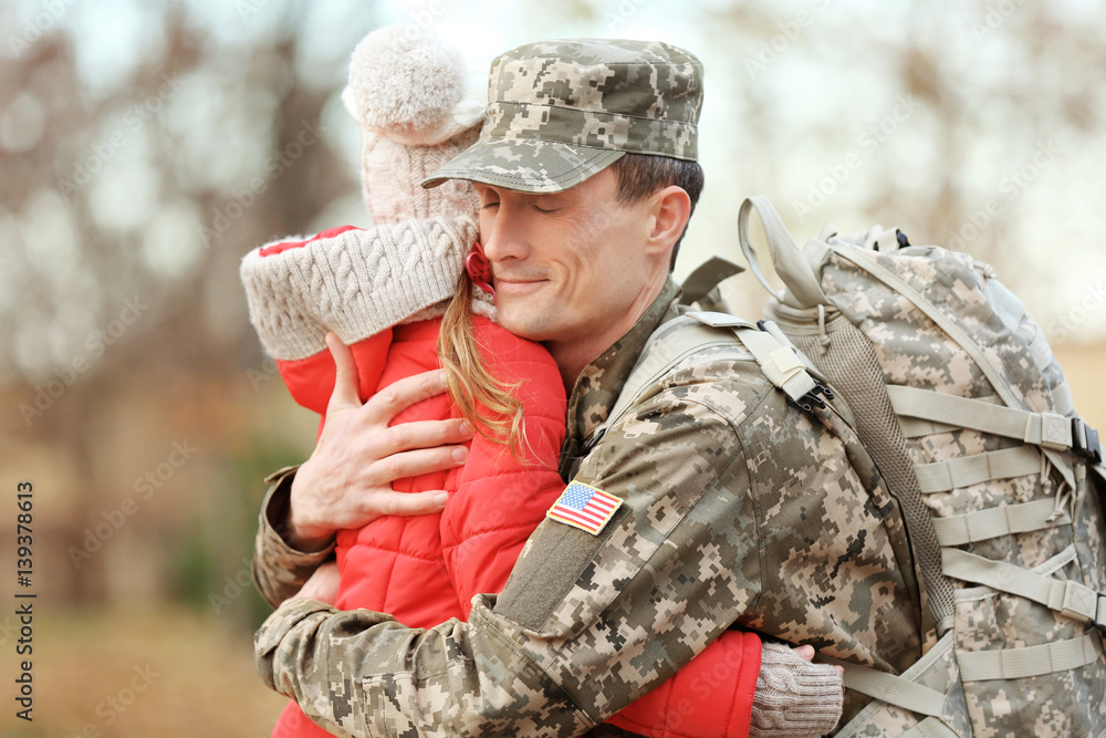 Soldier in camouflage hugging daughter outdoors