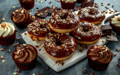 Wall Mural - donut rings and vanilla caramel cupcakes with white and dark chocolate chippings and icing served on board