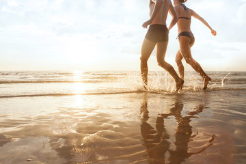 Wall Mural - happy young couple running to the sea on the beach at sunset, silhouettes of man and woman, family h