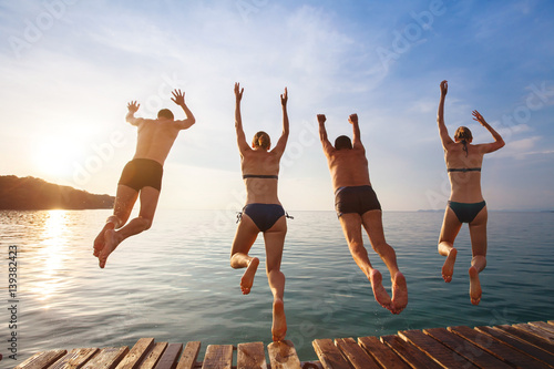 Foto group of friends jumping to the sea from the pier, happy beach holidays