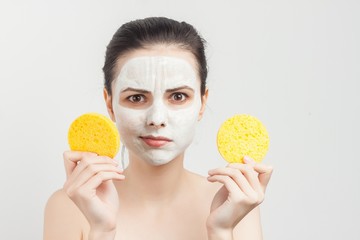 puzzled woman with white mask on face and two sponge in hand