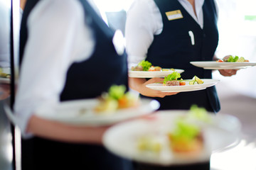 Waiter carrying plates with meat dish on some festive event