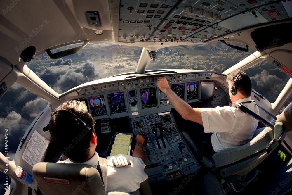 Flight Deck of modern passenger jet aircraft. Pilots at work. Cloudy sky and sunset view from the airplane cockpit. - obrazy, fototapety, plakaty 