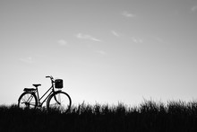 Silhouette Of Old Bicycle On Grass With The Sky Sunset, Color Black And White Tone And Soft Focus Concept Journey