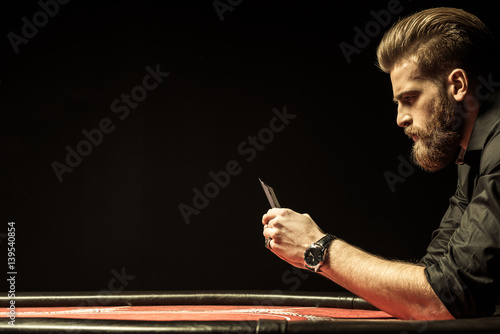 фотография Side view of bearded man holding poker cards on black