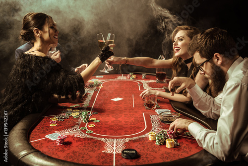 Fotografie, Obraz side view of women clinking drinks while playing poker in casino