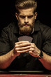 Serious bearded man holding poker cards on black