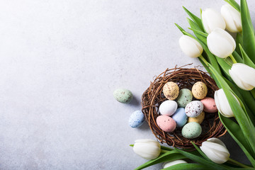 Wall Mural - Beautiful white tulips with colorful quail eegs in nest on light gray stone background. Spring and Easter holiday concept with copy space.