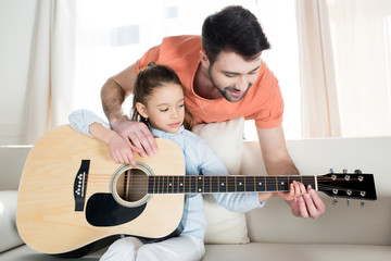 Wall Mural - Smiling father teaching little daughter playing guitar