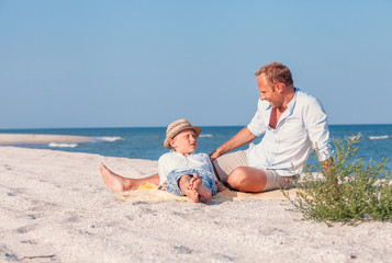 Wall Mural - Father with son take a sun bath on the sea beach