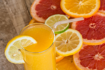 glass of orange juice on the wood background with slices of citrus