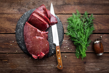 Raw liver on slate board on wooden background top view